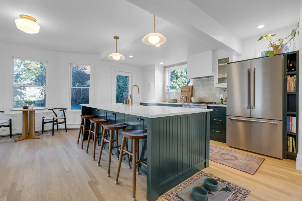 Green kitchen island with wood stools beside an open dining area