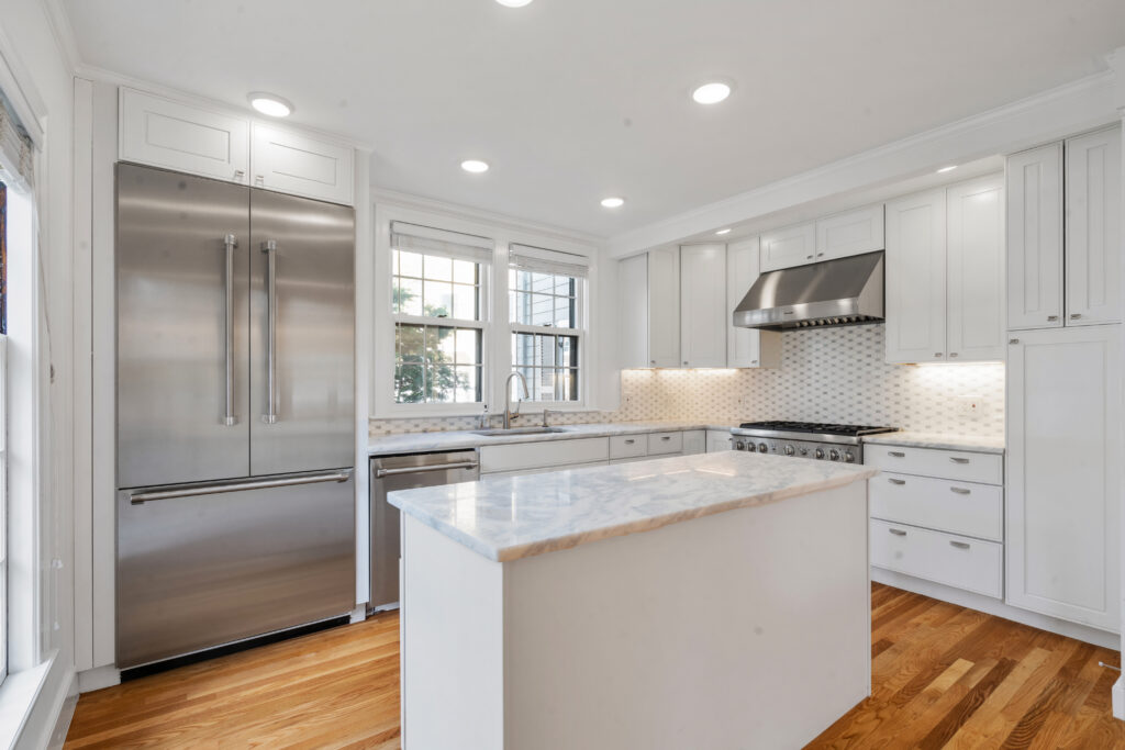 White kitchen with a marble-look island and large stainless steel refrigerator