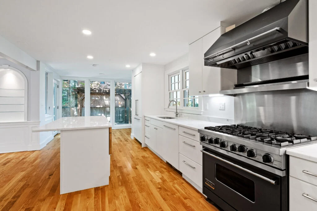 Long white kitchen island facing a stainless steel range